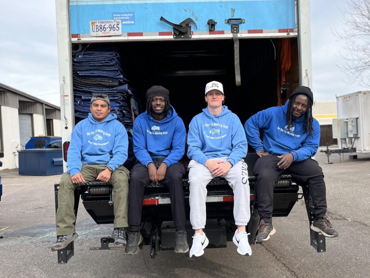 Four professional movers from On The Fly Moving Guys sitting at the back of a moving truck