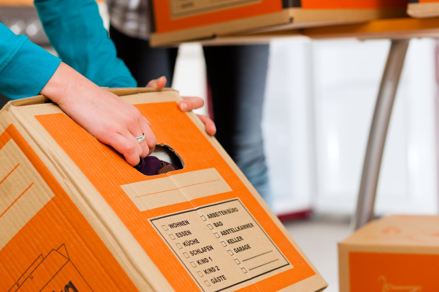 A hand holding an orange and brown moving box